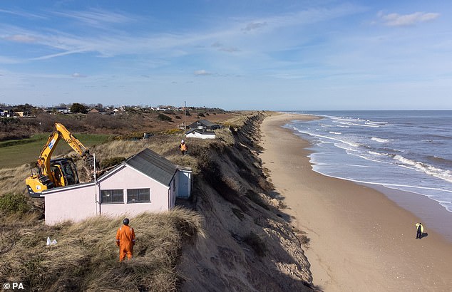 Homeowners were forced to look on as a digger moved in to destroy their clifftop houses that are inches away from toppling into the sea