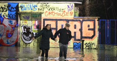 A couple make their way through floodwater at Hackney Wick in East London this morning