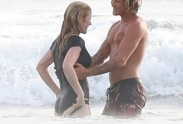Handsome surfing instructor Armando Perez holds a smiling Ellie close as the waves roll in