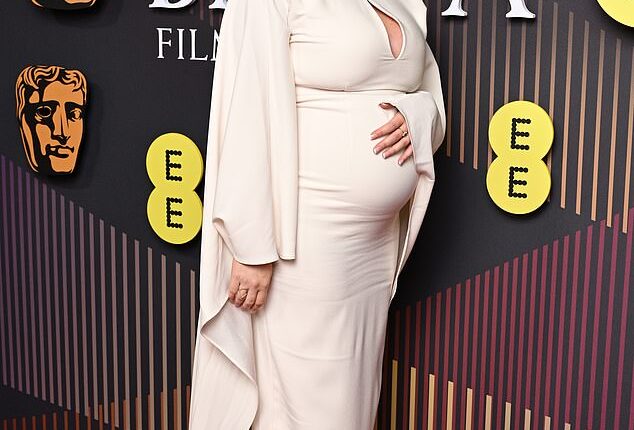 Pregnant Emily Atack cradles her baby bump in a flowing cream gown with keyhole cut out as she hit the red carpet on Sunday's BAFTAs ceremony