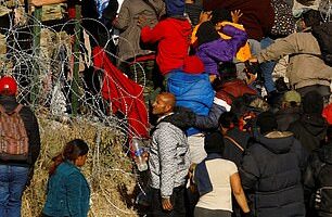 Migrants seeking asylum in the United States try to cross a razor wire fence on the Southern border