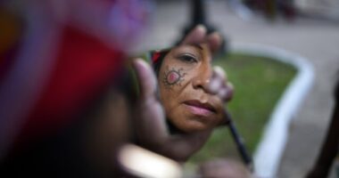 A Maka Indigenous woman puts on make-up before protesting for the recovery of ancestral lands in Asuncion, Paraguay, Wednesday, Feb. 28, 2024. Leader Mateo Martinez has denounced that the Paraguayan state has built a bridge on their land in El Chaco's Bartolome de las Casas, Presidente Hayes department. (AP Photo/Jorge Saenz)