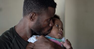 man holding his baby and giving her a kiss