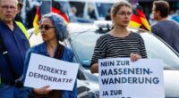 People hold banners that read "Direct democracy" and "No to mass immigration, yes to remigration" as far-right protesters march through the streets of Solingen