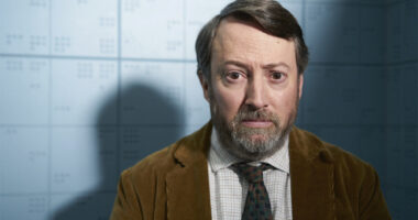 David Mitchell wearing a brown suit, white shirt and tie in BBC One series Ludwig