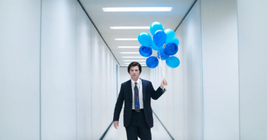 Mark S of Severance carrying blue baloons in hallway.