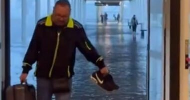 A man is seen taking his shoes off and wading through the departures hall at El Prat airport