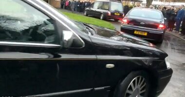 In footage of the funeral, onlookers stand by solemnly on the pavement as a hearse drives slowly past
