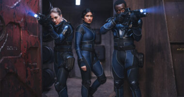 Three people in spacesuits holding guns on a mining base in space