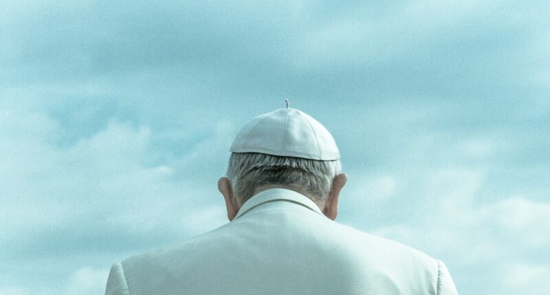 The pope from behind, a person in a white cap