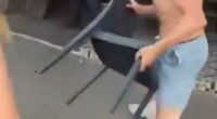 One of the brawling teens, a topless male, picks up a chair from outside the restaurant