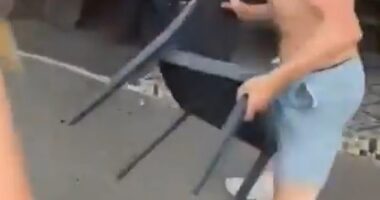 One of the brawling teens, a topless male, picks up a chair from outside the restaurant