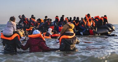 Migrants in the channel wading into water with children on their shoulders attempting to get on an inflatable boat