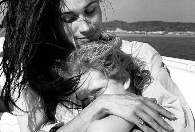 The Duchess of Sussex shared the black and white photo of herself cuddling Princess Lilibet, who was sat on her lap, with the pair both sporting windswept hair, seemingly on a boat