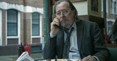 Gary Oldman in a dirty suit and tie on his mobile phone and eating a full English breakfast as Jackson Lamb in Slow Horses