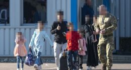 A soldier escorts a family at Stansted on May 23 as part of a government scheme costed at £7billion smuggling migrants TO Britain after a data-leak blunder exposed by the Daily Mail