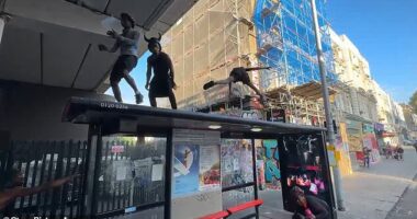 Three men splattered in paint were spotted dancing on top of a bus stop outside Ladbroke Grove station, near Portobello Road market