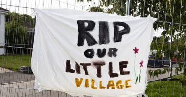 A banner which reads 'RIP our little village' hung on the railings put up around the new developments