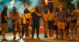 Protesters wearing masks and balaclavas hold chains, sticks and baseball bats during the fourth night of riots on July 14, 2025 in Torrepacheco, in the province of Murcia, Spain
