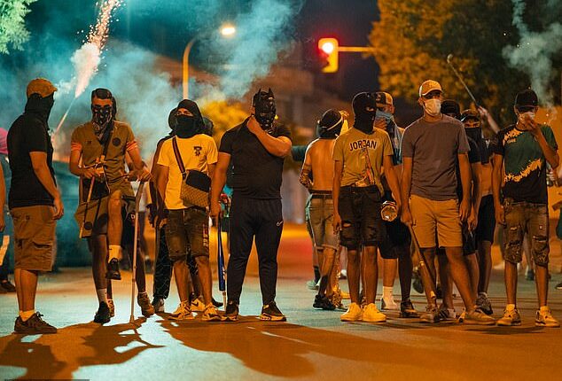 Protesters wearing masks and balaclavas hold chains, sticks and baseball bats during the fourth night of riots on July 14, 2025 in Torrepacheco, in the province of Murcia, Spain