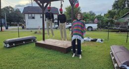 The display consists of two figures wearing plain red hats, black shirts and face masks, and khakis with zip ties stuffed in the front pockets. Both are hanging from a noose. Another mannequin wearing a colorful poncho