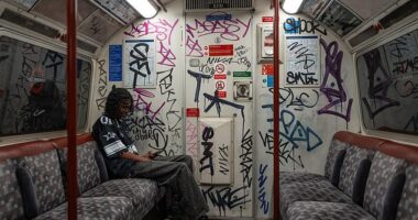 A London Underground passenger sits in a Bakerloo Line carriage covered in graffiti in June