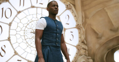 Ncuti Gatwa in a blue and white outfit standing in front of a clock in Doctor Who