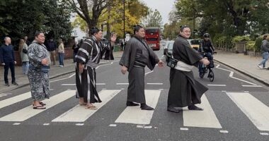 Four wrestlers can be seen in traditional dress proudly striding across the zebra lines, with a London bus and cyclists in the background