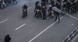 A photo of a lone demonstrator defiantly sitting on the road in front of armed security forces in Iran has gone viral on social media