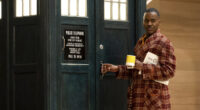Ncuti Gatwa wearing a tartan dressing gown and holding a cup of tea standing by the TARDIS
