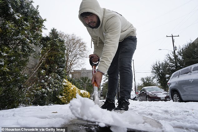Pictured: A hotel worker in Houston, Texas, shovels snow off a sidewalk after a storm on January 21, 2025
