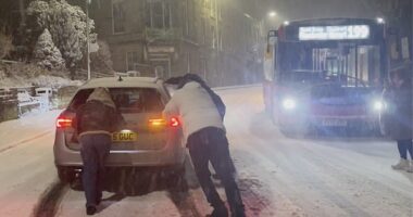 People attempt to push a car stuck in the snow in Buxton, Peak District, Derbyshire, on Thursday night
