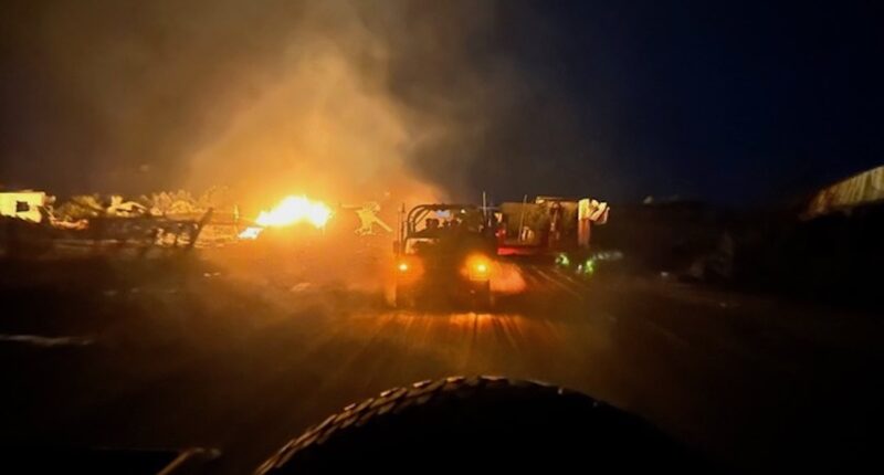 vehicle drives past fiery war scene at night