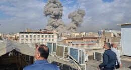 People watch as smoke rises on the skyline after an explosion in Tehran, Iran