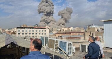 People watch as smoke rises on the skyline after an explosion in Tehran, Iran