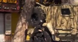 In the footage, an IRGC military member holds a gun and is flanked by the regime's signature light yellow massive truck