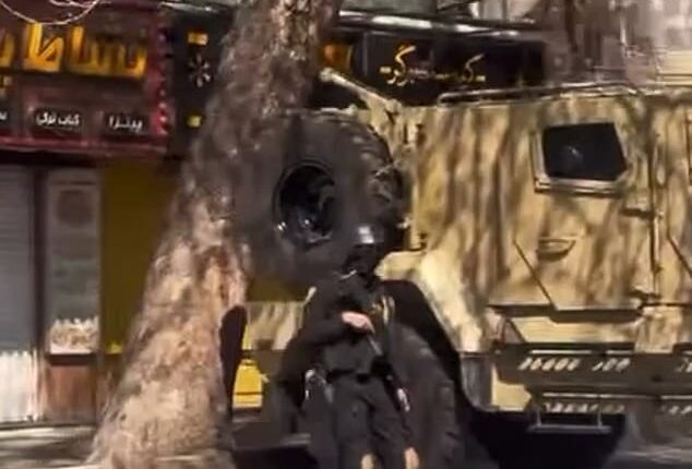 In the footage, an IRGC military member holds a gun and is flanked by the regime's signature light yellow massive truck