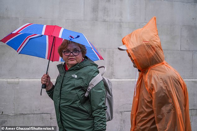 People in Trafalgar Square shelter under an umbrella while it is 'raining cats and dogs' (raining heavily)