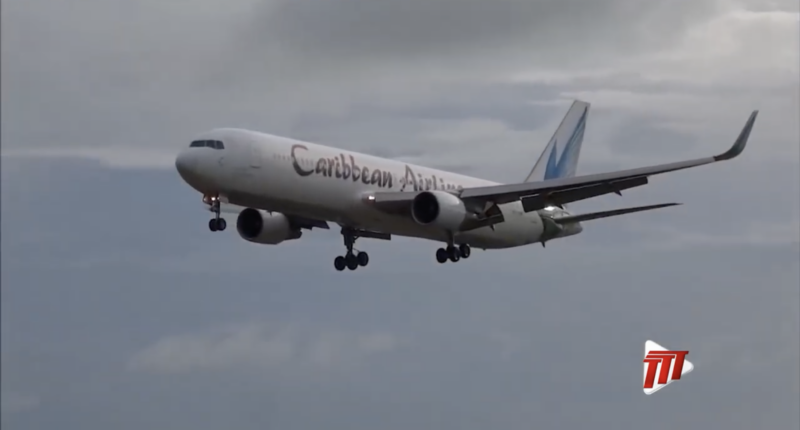 A Caribbean Airlines jet flies through cloudy skies.