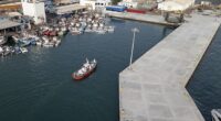 An aerial view of an ambulance boat carrying crew members wearing hazmat suits as they arrive at the port after approaching the pilot door on the starboard side of the cruise ship MV Hondius, while stationary off the port of Praia, the capital of Cape Verde, on May 5, 2026