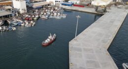 An aerial view of an ambulance boat carrying crew members wearing hazmat suits as they arrive at the port after approaching the pilot door on the starboard side of the cruise ship MV Hondius, while stationary off the port of Praia, the capital of Cape Verde, on May 5, 2026