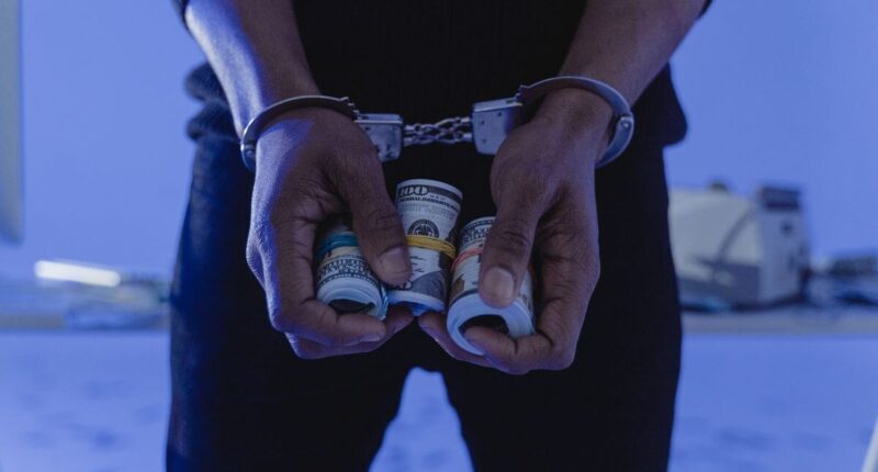 Person in handcuffs holding rolls of money.