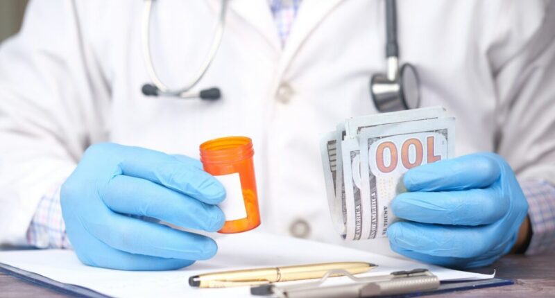 Doctor holds empty pill bottle in one hand and money in the other.