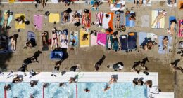 People sunbathe and swim at London Fields Lido in London on Tuesday afternoon