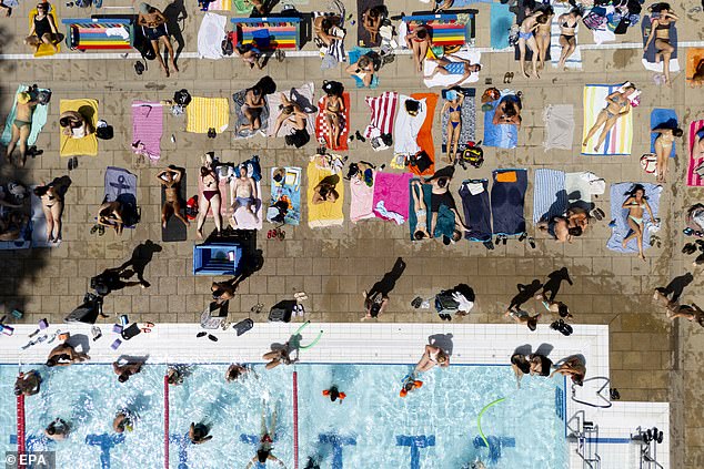 People sunbathe and swim at London Fields Lido in London on Tuesday afternoon
